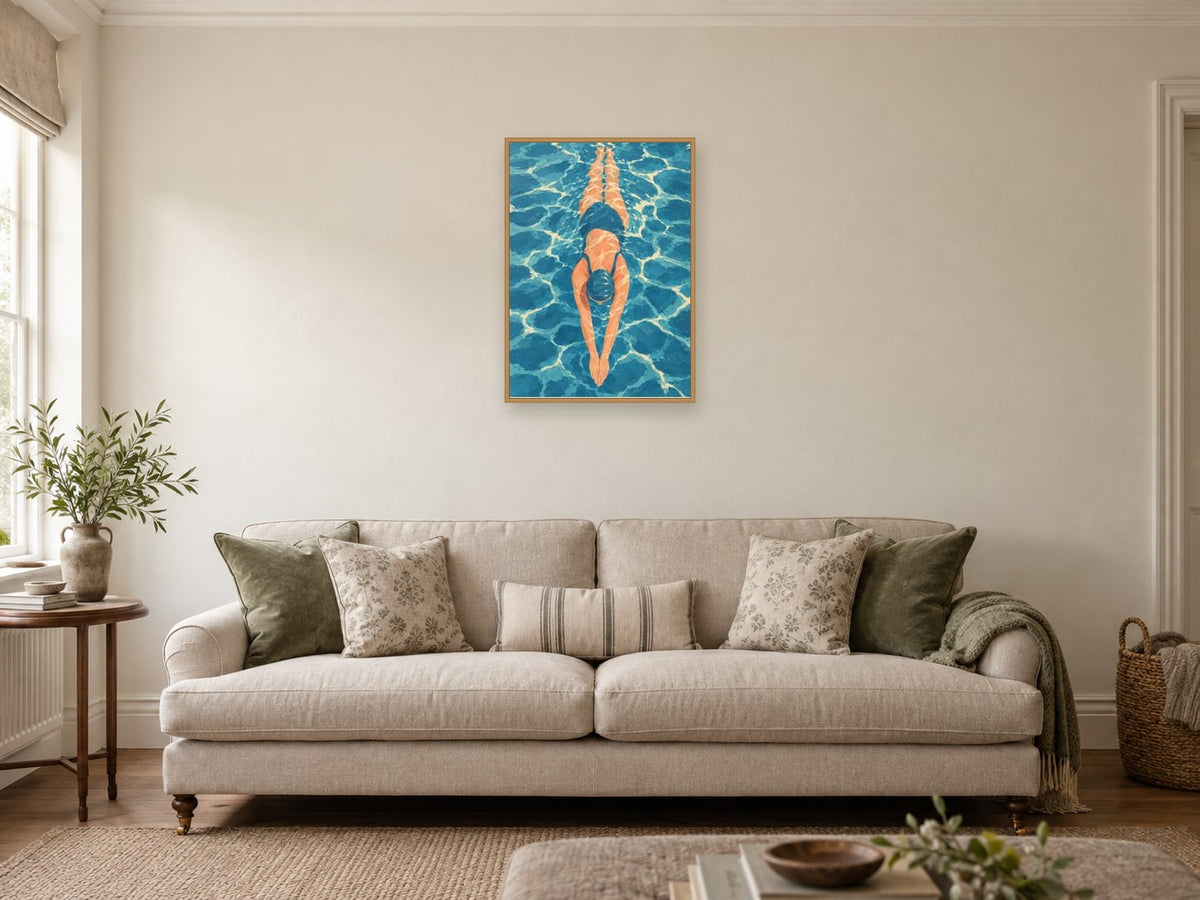 Swimmer seen from above in clear blue water — A2 artwork shown in a room with a natural wood frame; select a framed finish to include a frame